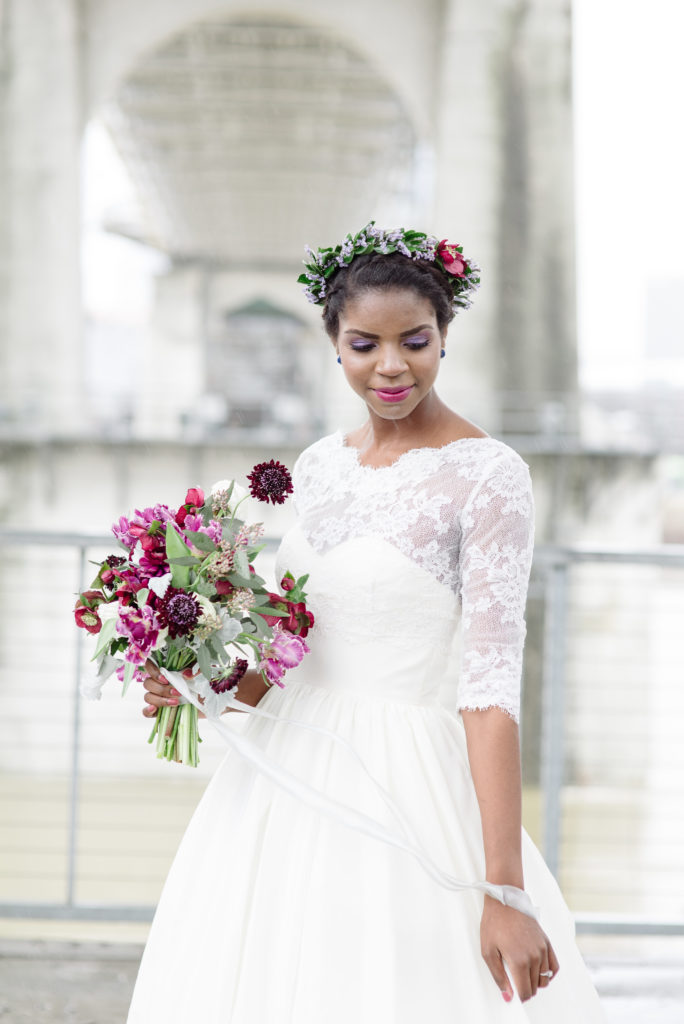 Black Bride is wearing a floral crown and is holding her wedding dress with one hand and is looking down and smiling for her bridal portraits