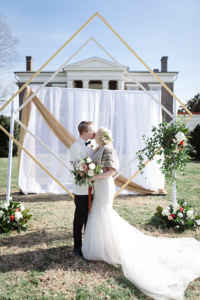 Newly Wed Husband and Wife are kissing in front of a gorgeous arbor in an outdoor wedding in January