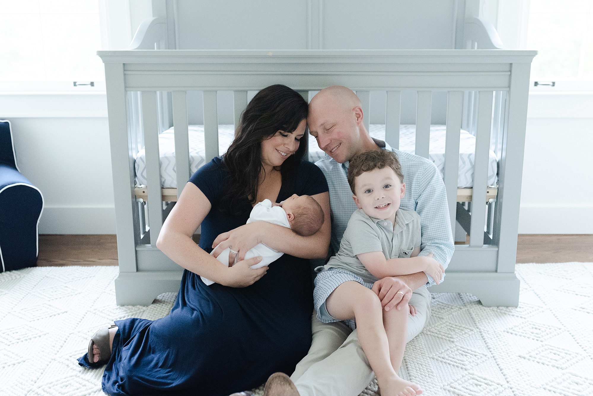 Family of four sitting in a nursery and taking family portraits to celebrate the arrival of newborn son