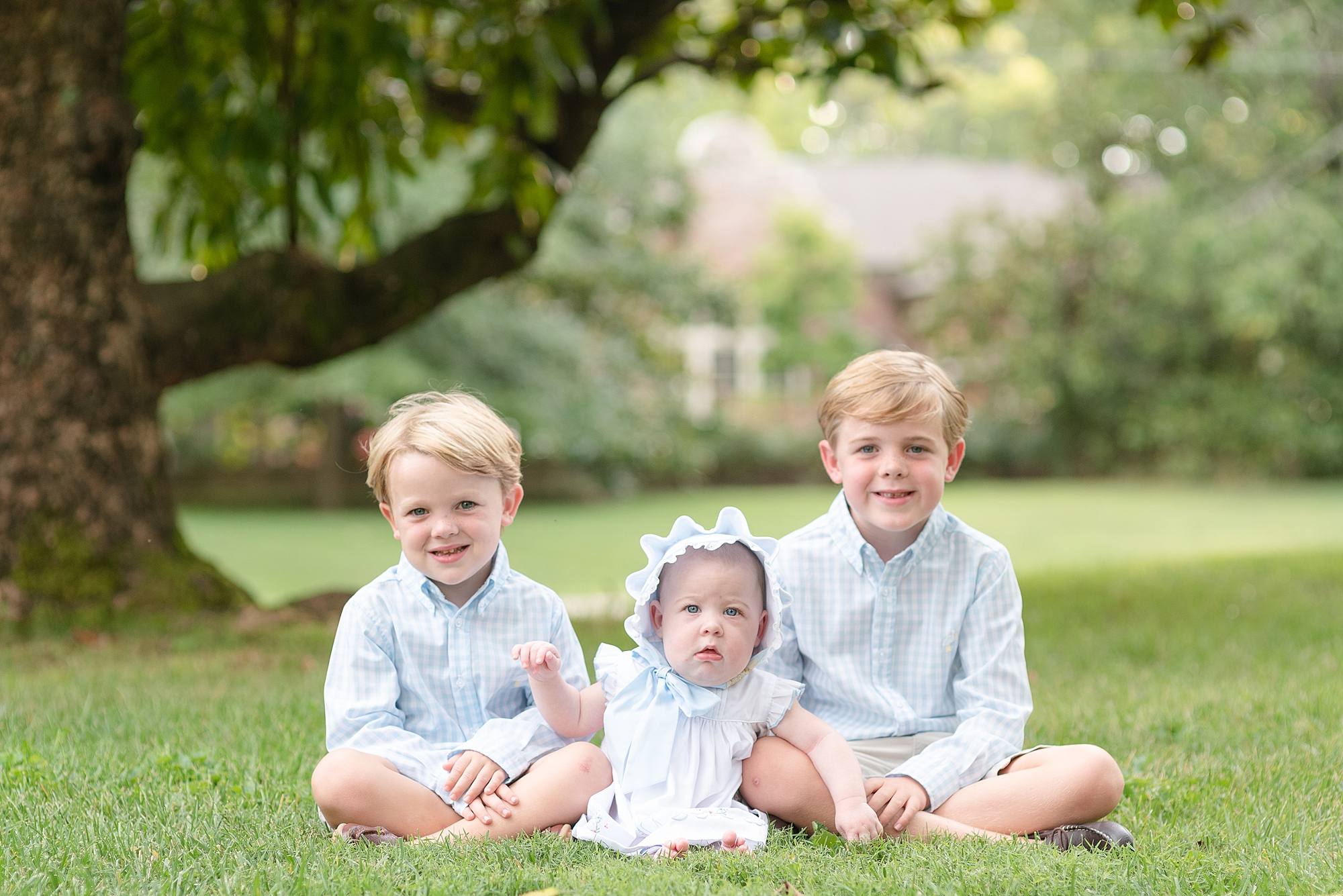 Three siblings are sitting on the grass and are looking at the camera