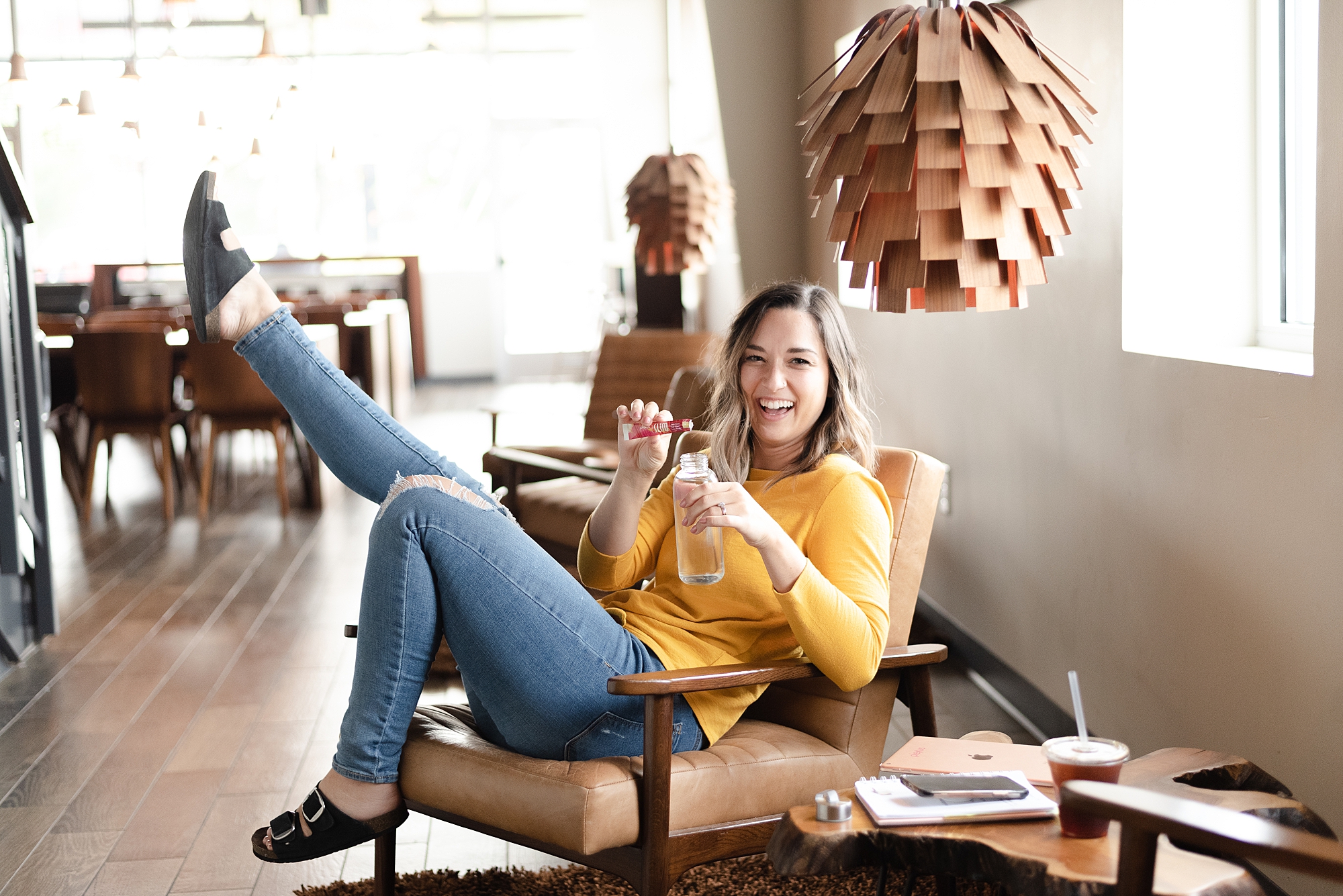 Joyful Woman Wearing a Yellow Shirt is sitting in a coffeeshop and is pouring herself a plexus pink drink and laughing