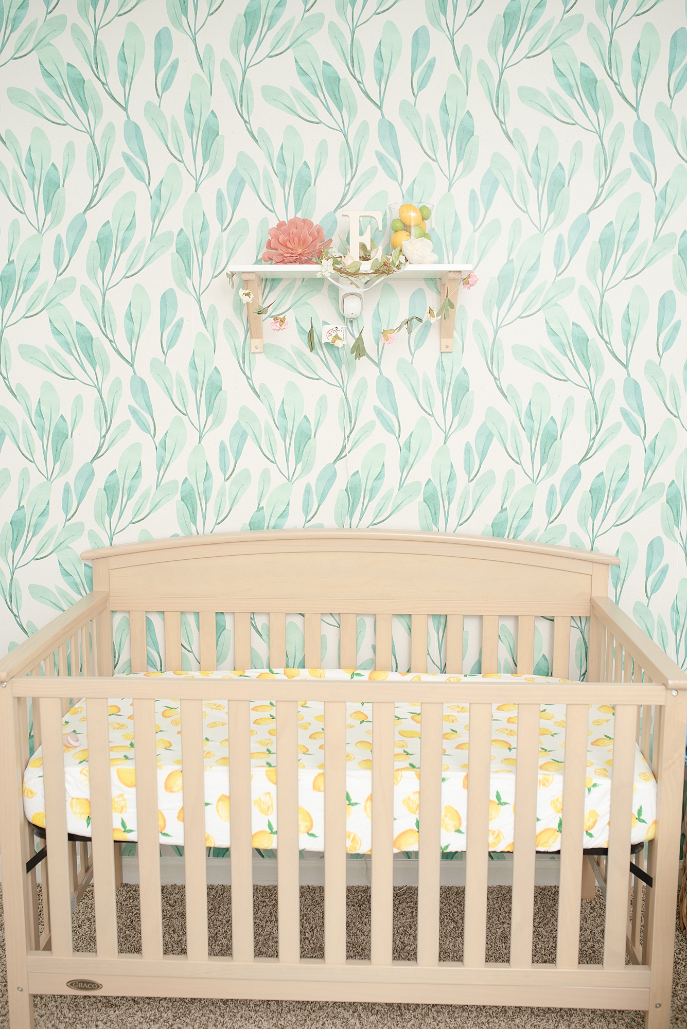 Modern Nursery Decor Details of a girls nursery in Nashville featuring a neutral wooden crib with green leaf print wall paper in the background