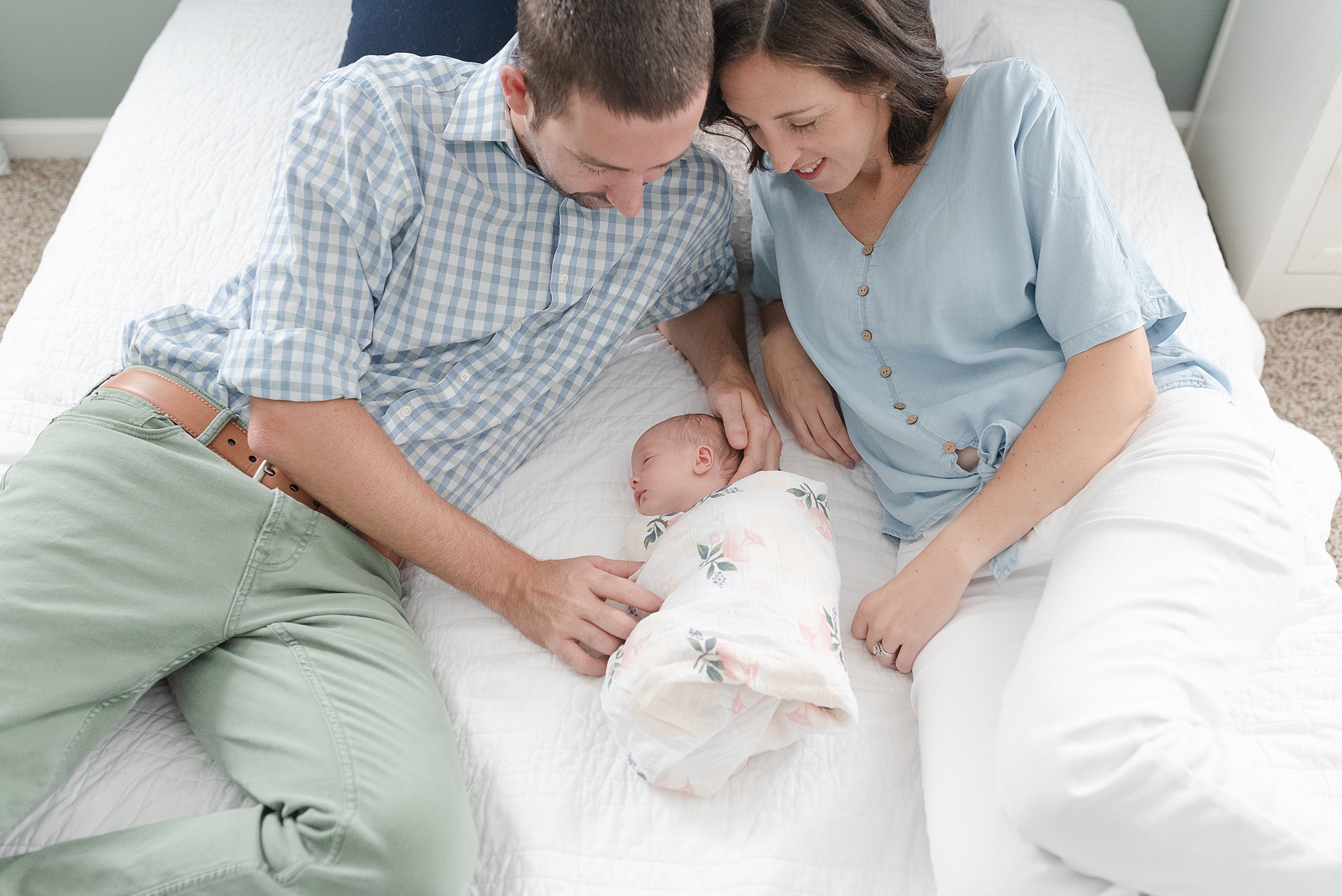 New mom and dad are looking down at newborn daughter and smiling in their bright bedroom