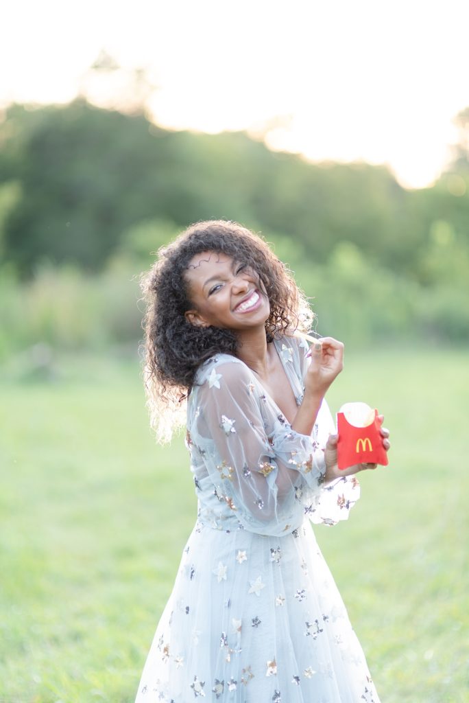 african american woman wearing a gorgeous stardust dress in the evening in Nashville TN and she is smiling real big and eating mcdonald's french fries