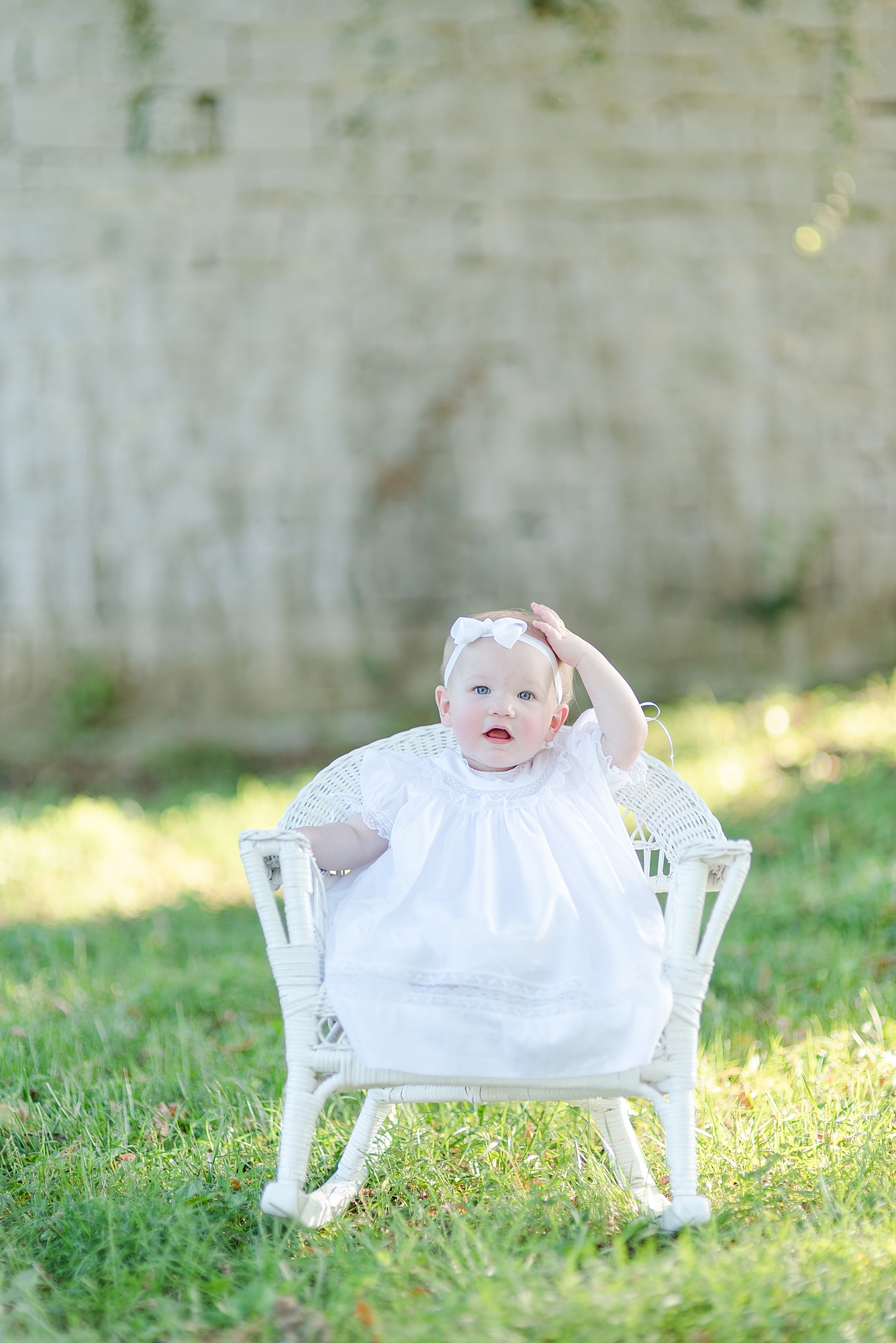 One Year Old wearing a white dress sitting in a wicker chair for her One Year Portraits in Nashville, TN