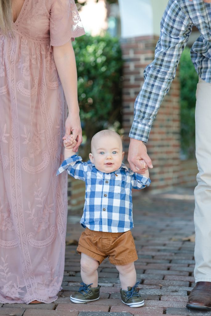 5 month portraits of a boy standing between his parents who are holding his hand as he tries to walk