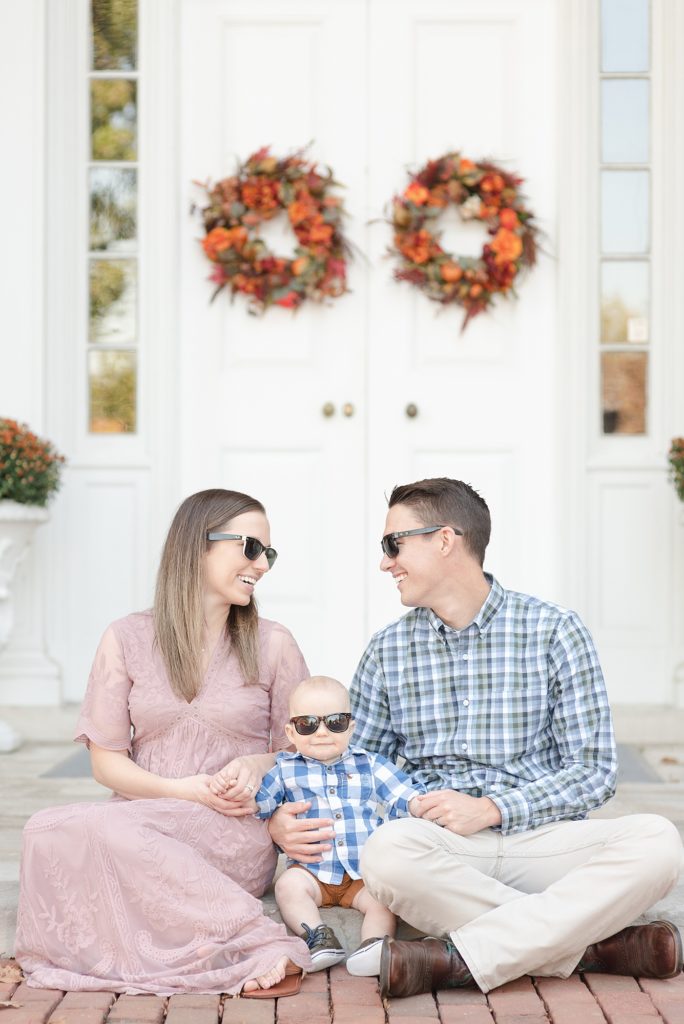 Family of three sitting down in front of a fall garland and they are wearing sunglasses for fun