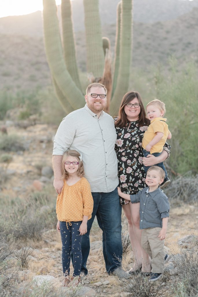 A family of five stands and smiles for their family portraits in the desert of Arizona at the base of the White Tank Mountains for their Christmas Portraits