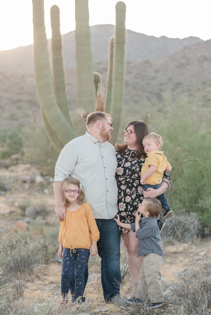 A family of five stands and smiles for their family portraits in the desert of Arizona at the base of the White Tank Mountains for their Christmas Portraits