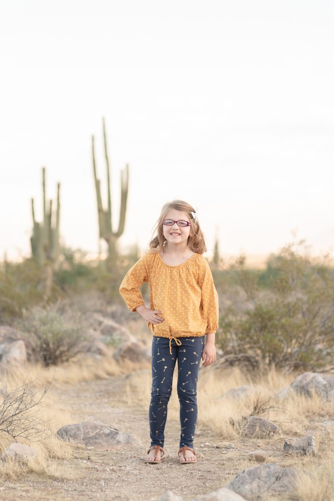 A young girl has her hand on her hips and is smiling at the camera for her christmas portraits in the desert