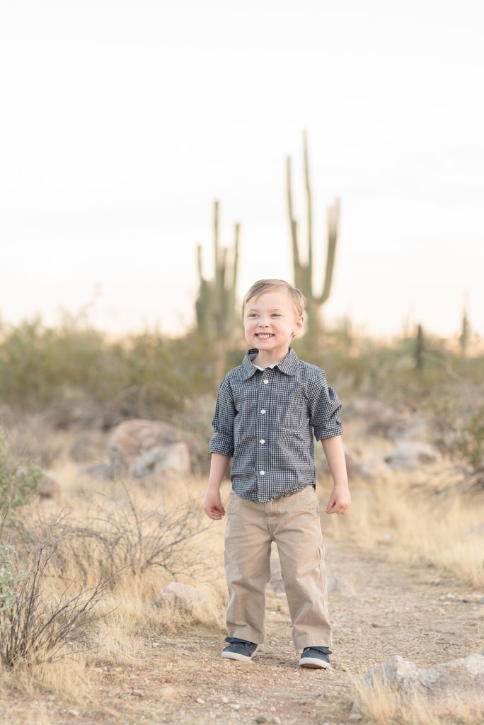 A young boy is smiling up at the camera for his christmas portraits in the phoenix arizona desert at the base of the White Tank Mountains