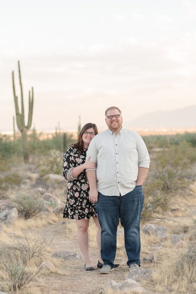 A husband and wife are snuggling together for portraits in the desert in Phoenix Arizona at the base of the White Tank Mountains by Dolly DeLong Photography