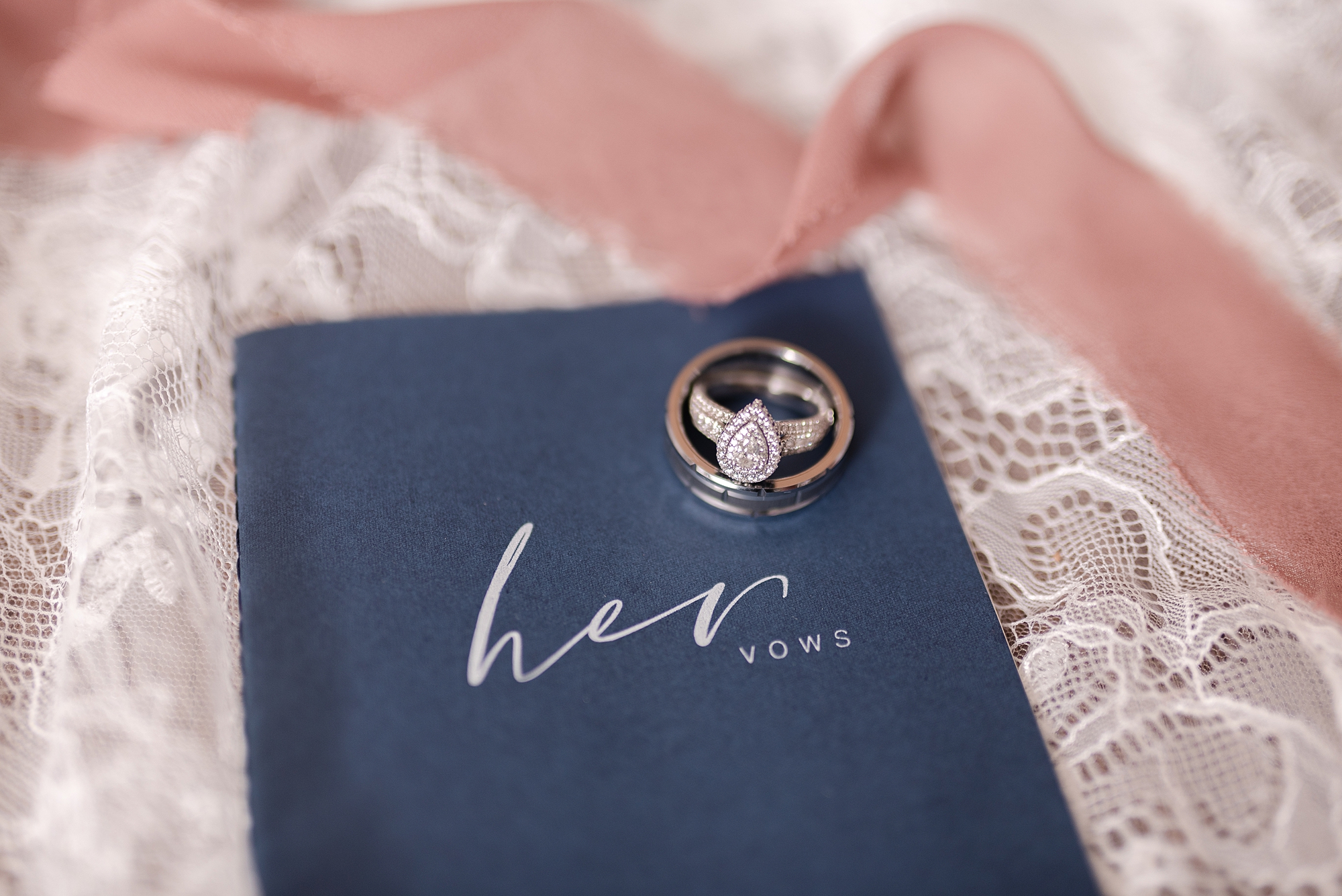a wedding day detail shot of the bride and grooms wedding rings on a vow book which is navy