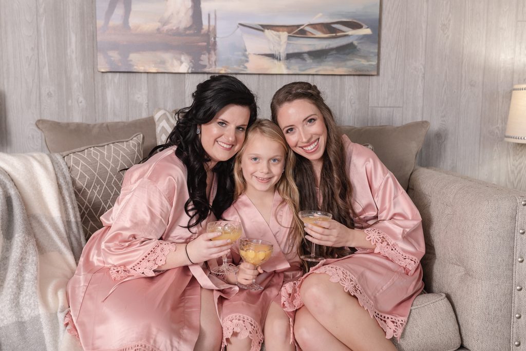 bridesmaids all sitting together on a couch wearing pink blush robes and smiling at the camera for a fall southern wedding