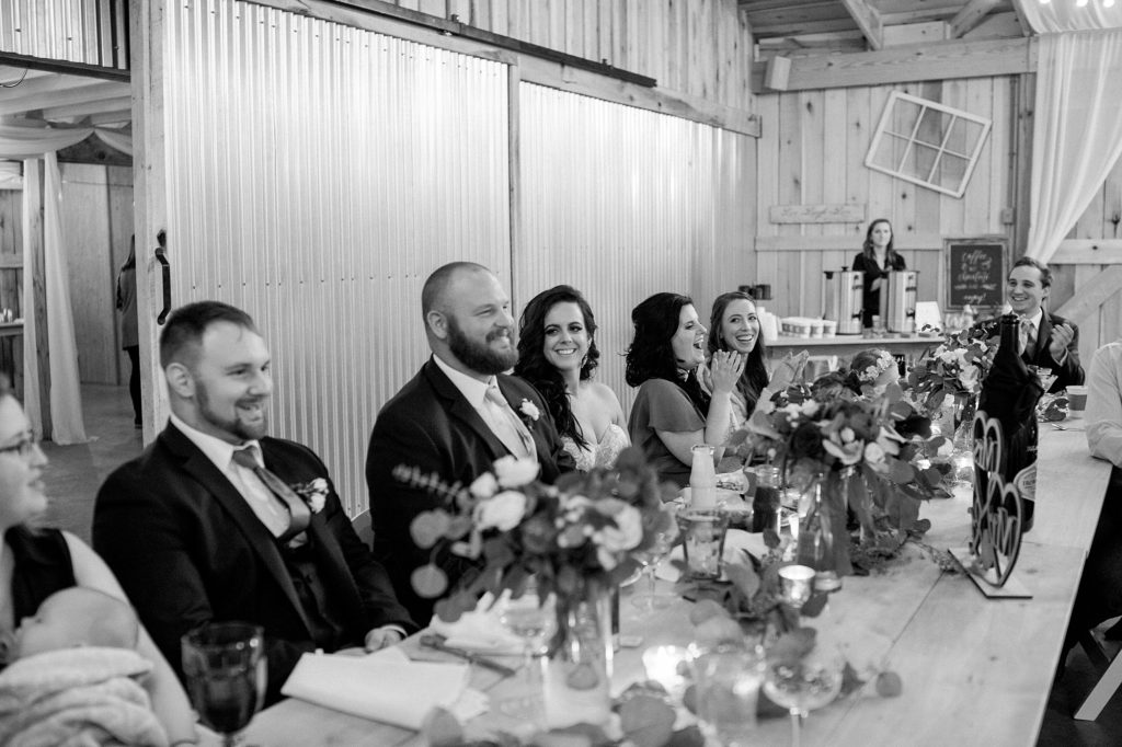 a black and white portrait of a bride and groom laughing at their reception during the speeches