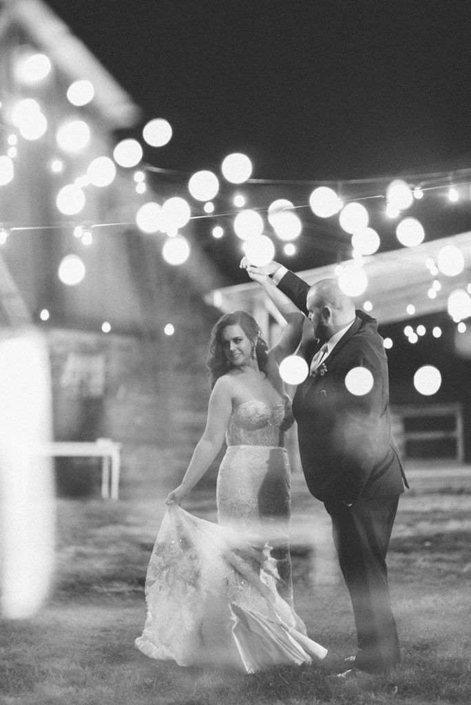 a black and white portrait of a bride and groom dancing together in the twinkling lights of a barn for their charming southern wedding in Nashville