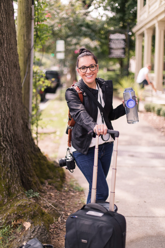 a woman in a black leather jacket is holding a water bottle and smiling at the camera in franklin tennessee for portraits 