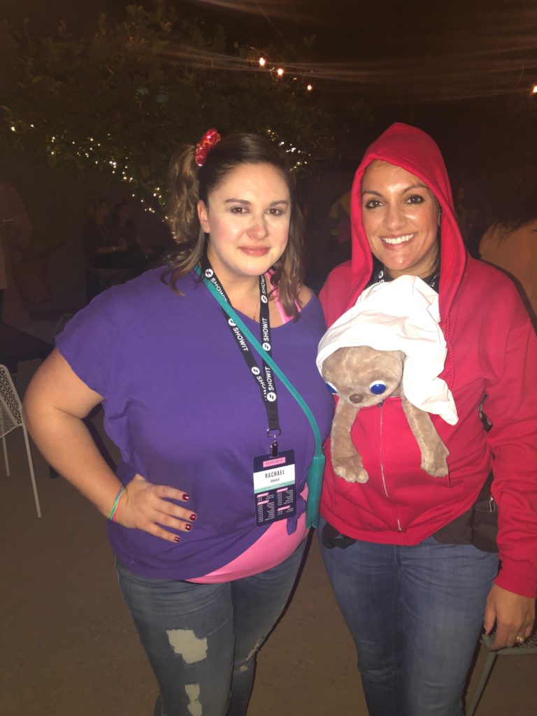 A woman dressed up from the 80s is standing next to a woman dressed up as E.T.