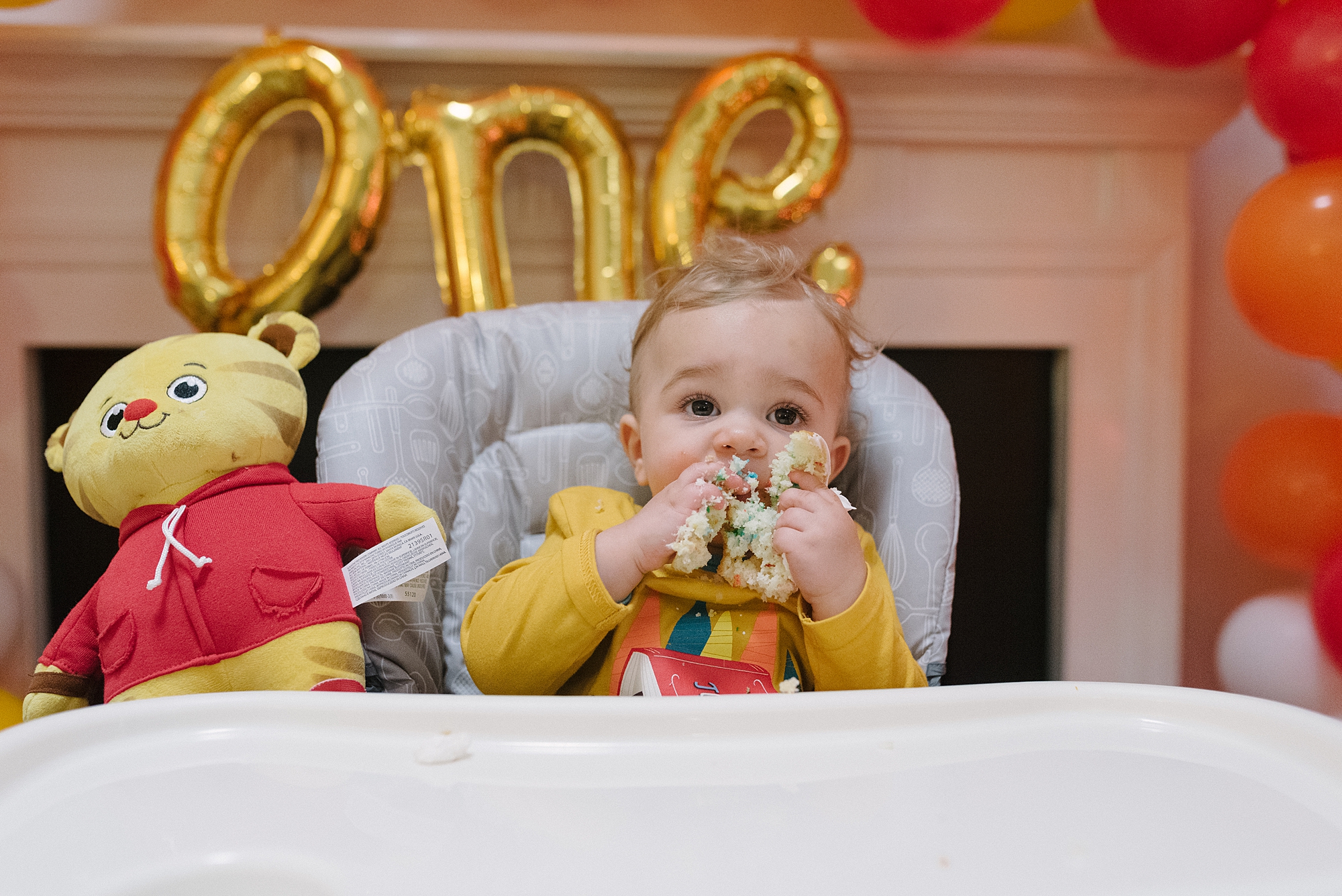 a one year old boy eating a cupcake at his daniel tiger themed birthday party