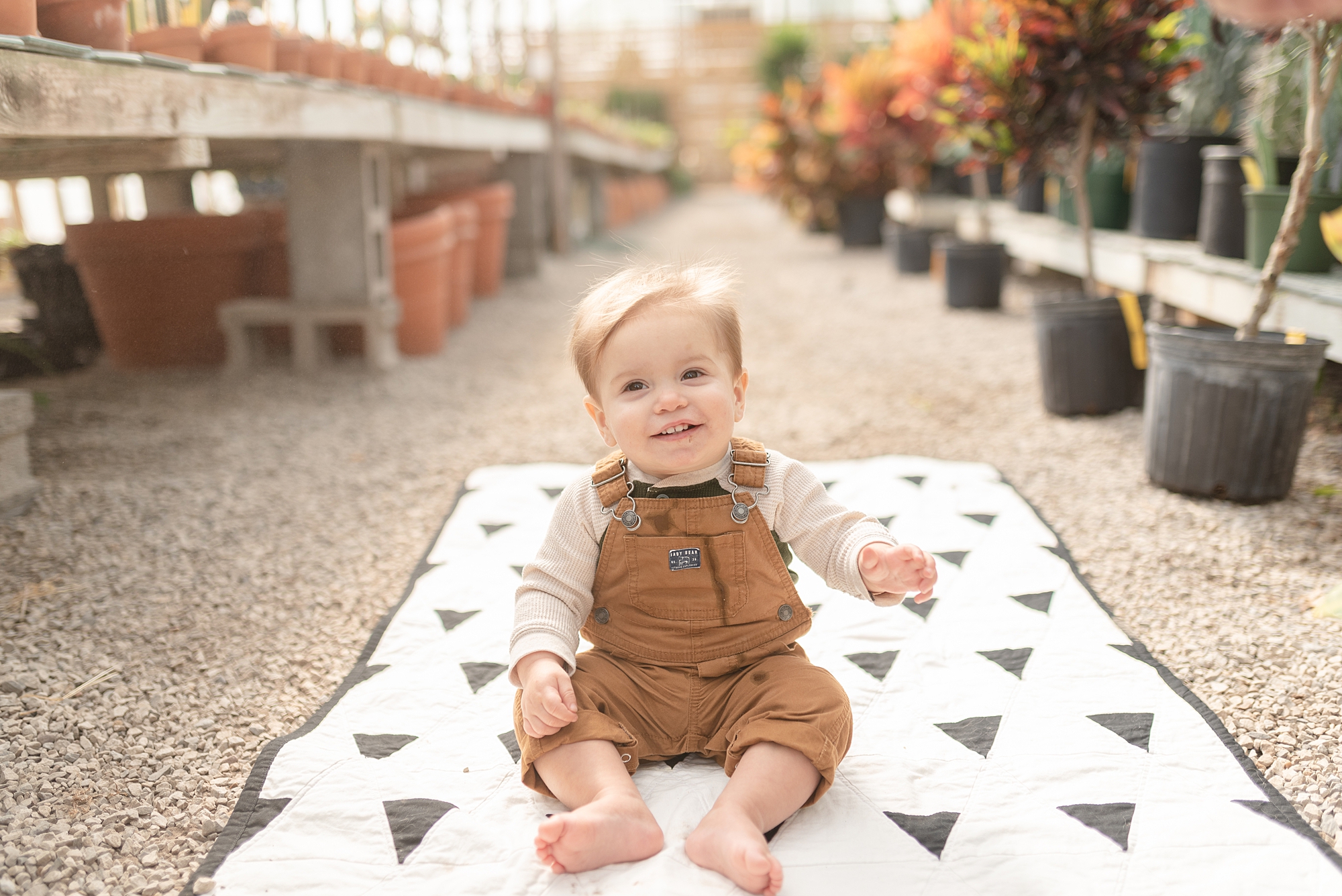 a boy sitting on top of his quilt for his one year milestone portraits at hewitt garden center in franklin