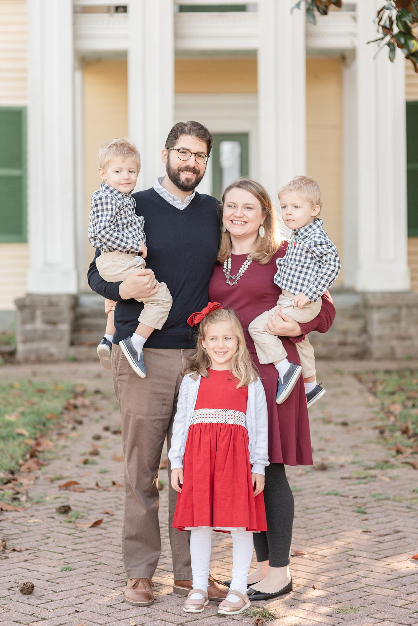 a family of five including twins and an older sister are standing in front of a yellow house in Nashville for family portraits