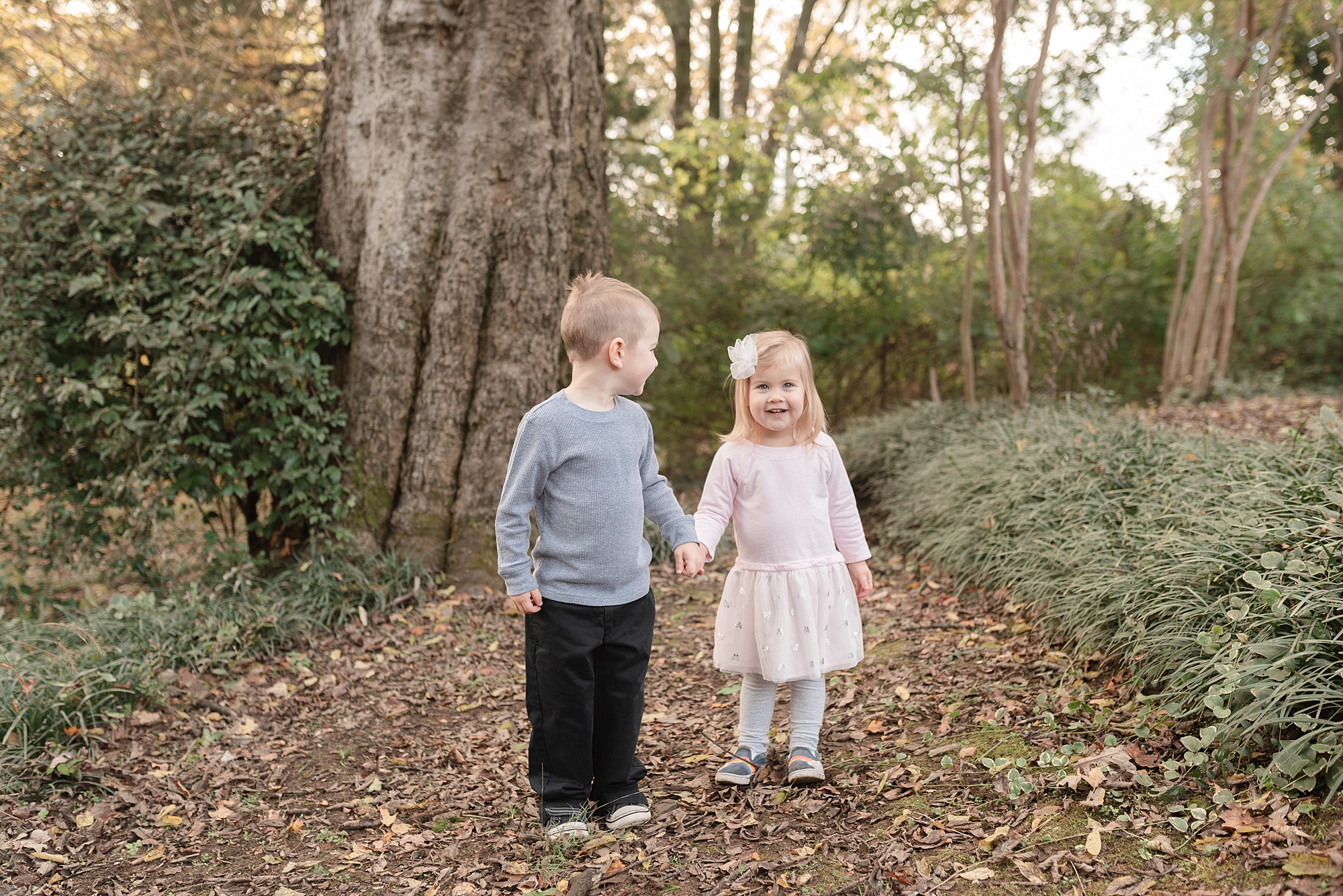 a brother and a sister are holding hands in front of a tree
