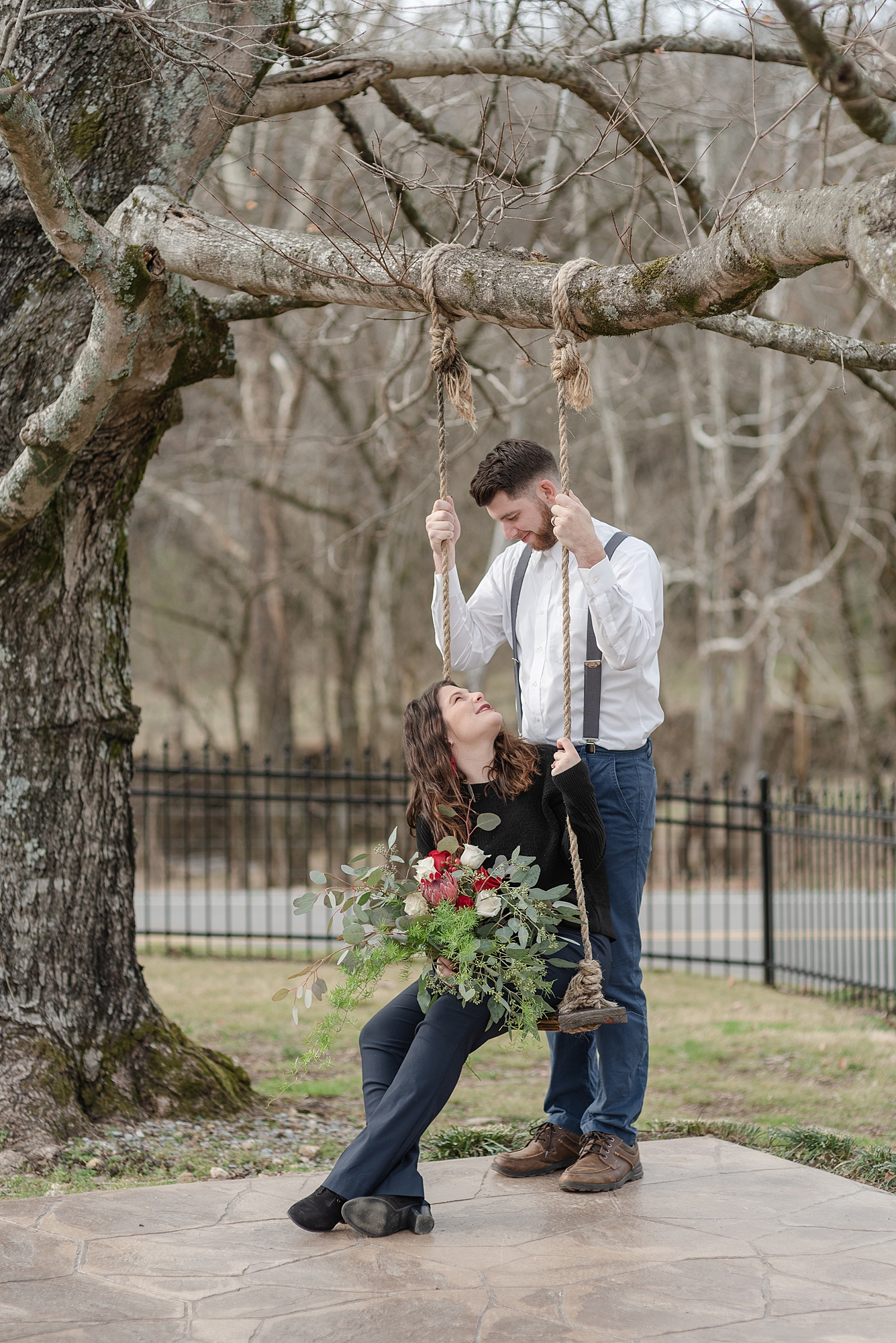 husband is looking down to his wife who is sitting on a swing while holding flowers at Promise Manor
