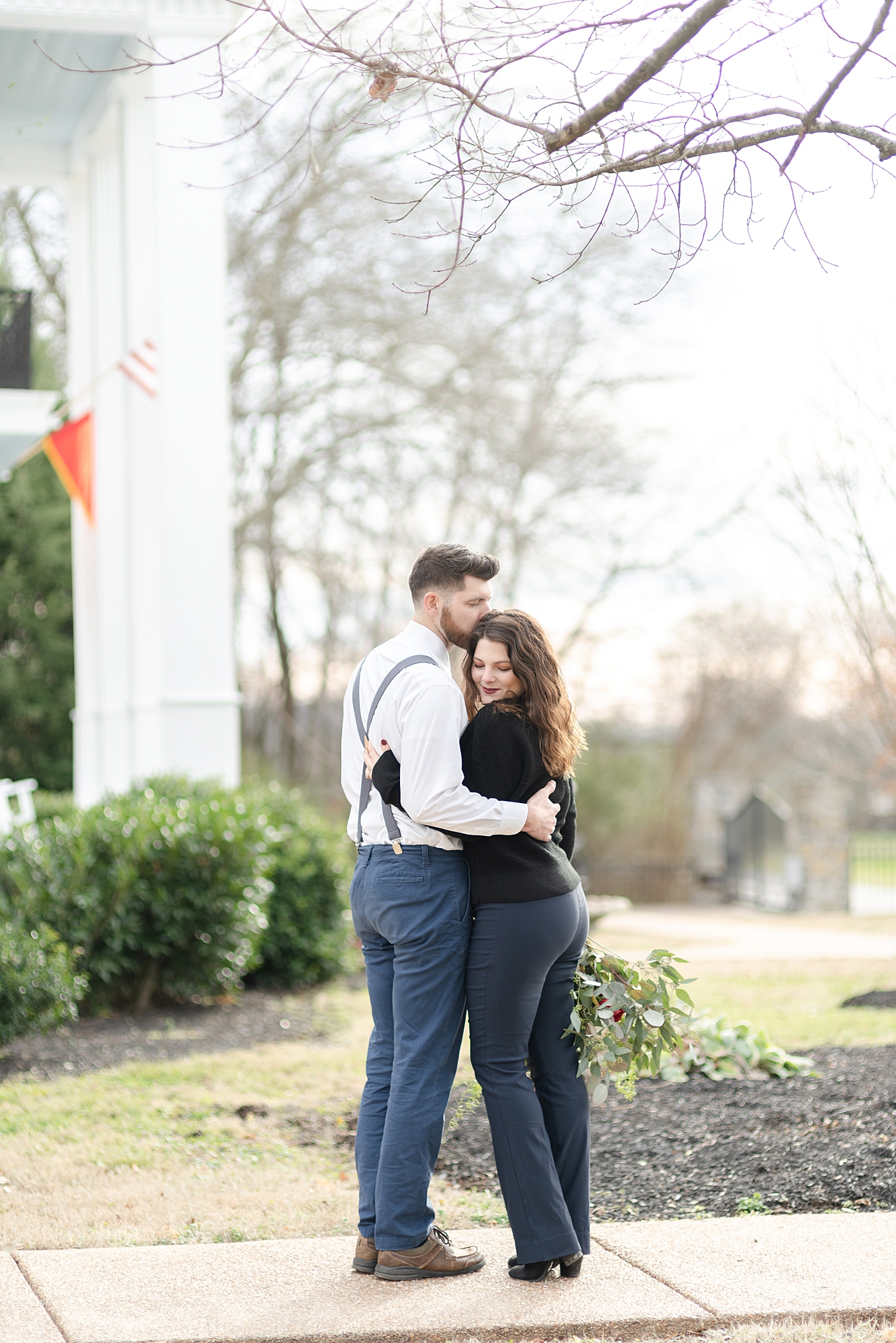 husband and wife holding eachother close and kissing eachother in front of promise manor by Dolly DeLong Photography
