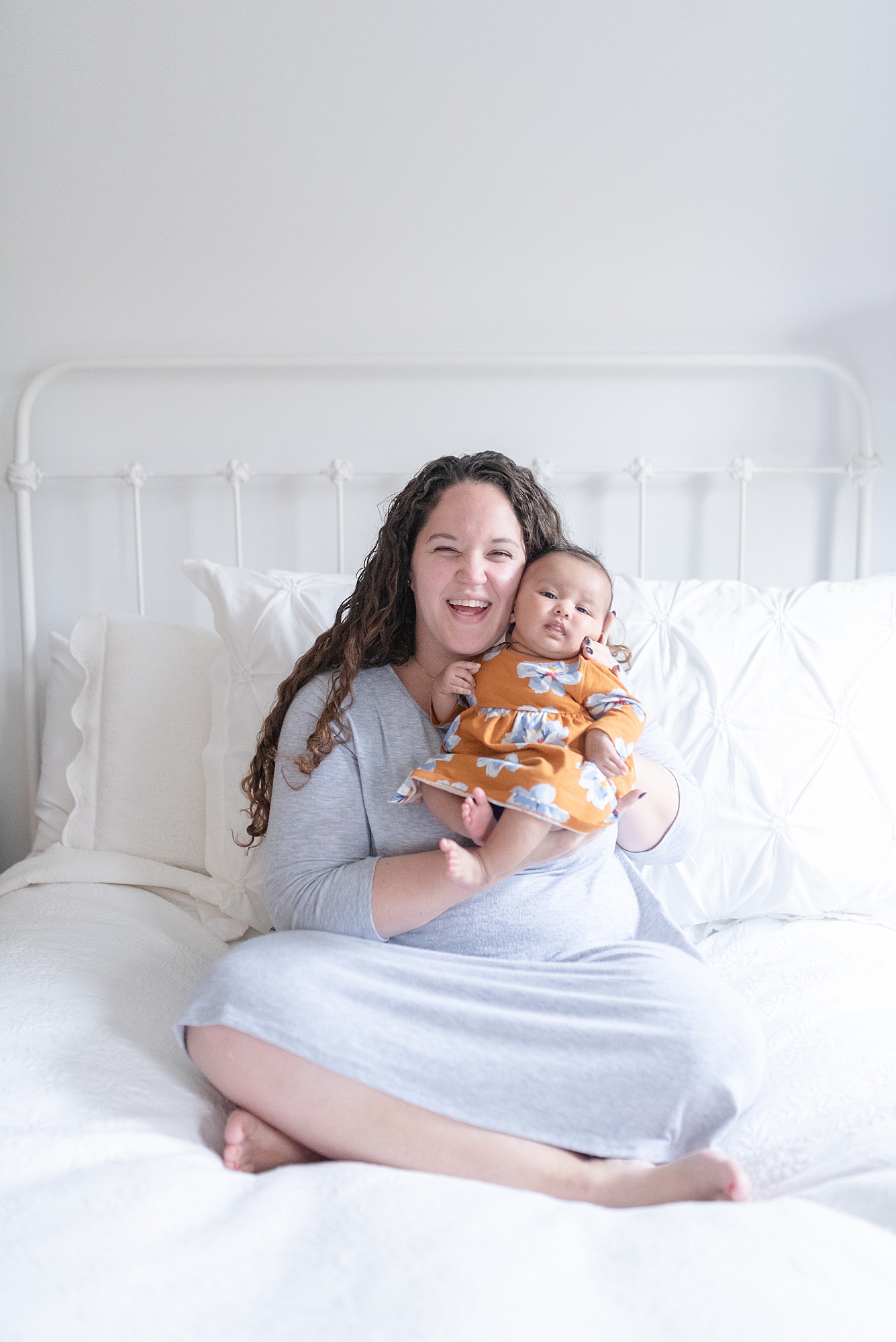 new mom is looking down and smiling at her baby girl while sitting on a white bed for family photos in Nashville