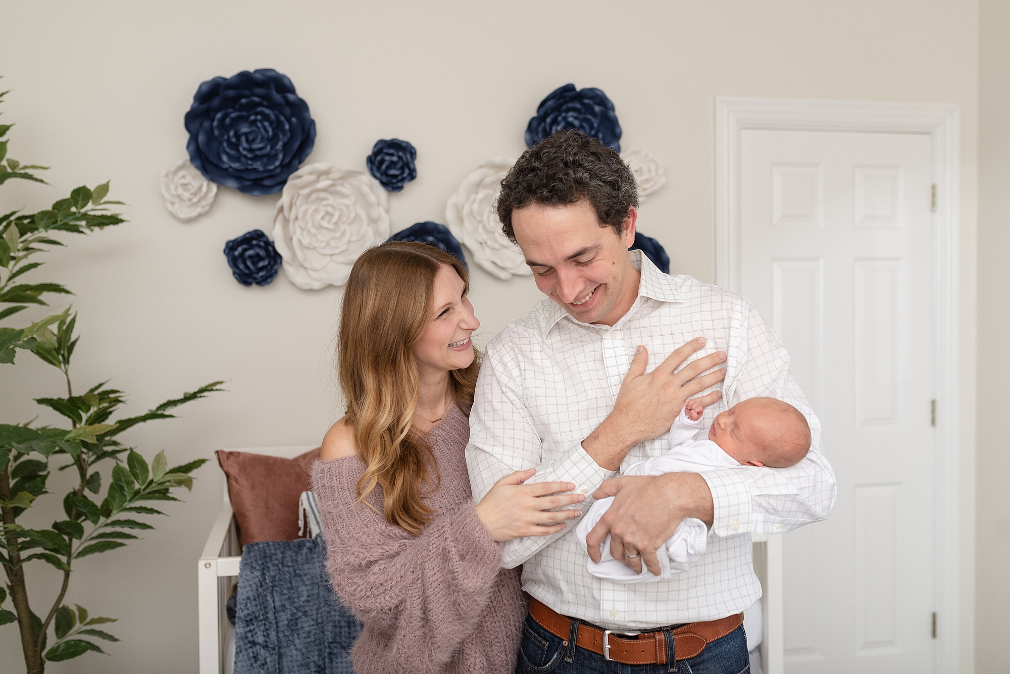 mom and dad are holding baby girl for family photography session in Nashville in the newborn girl's nursery and laughing