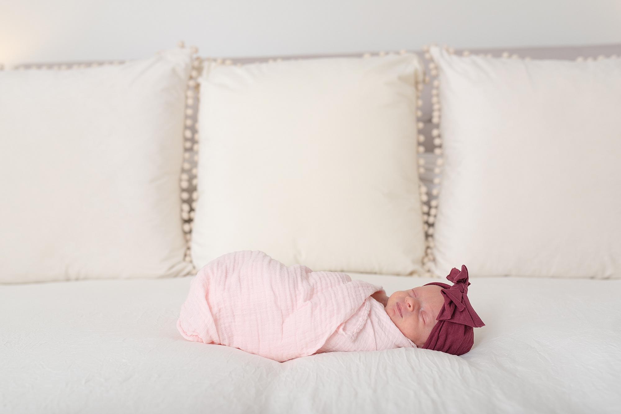 a newborn baby is wrapped up in a pink swaddle and sleeping in the middle of a white bed in Nashville by Nashville family photographer Dolly DeLong Photography