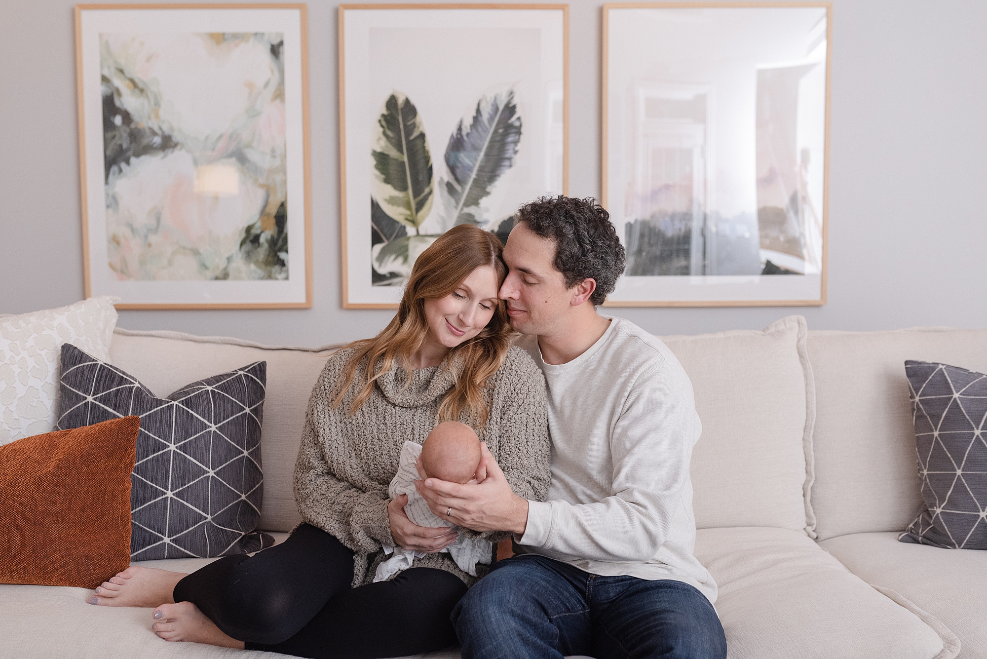 mom and dad sitting on their couch in their living room and holding their newborn baby girl in Nashville by Nashville family photographer Dolly DeLong Photography