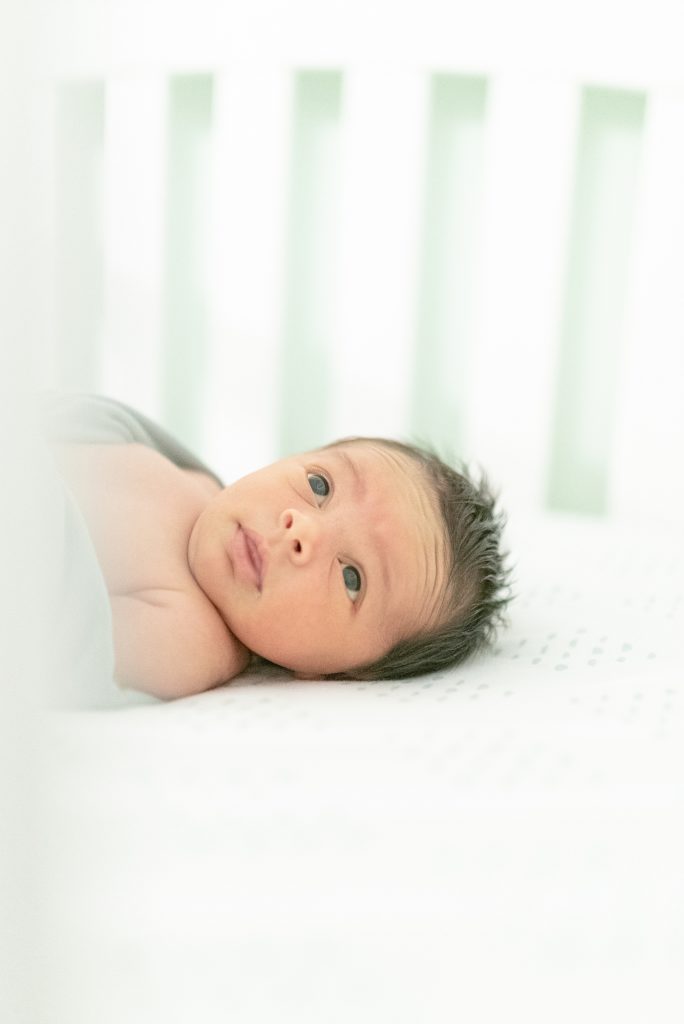 a newborn daughter in her crib and she is looking up at her mommy and daddy by nashville newborn and family photographer Dolly DeLong Photography