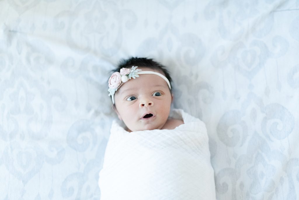 a newborn baby girl is swaddled up in a white swaddle and is wearing a floral bow at a newborn and family session by nashville family photographer Dolly deLong Photography