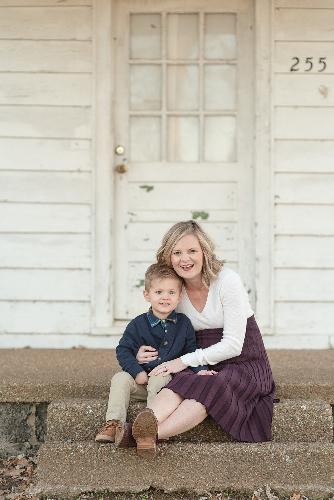 A mother and young toddler son are sitting on the front porch together and snuggling and smiling for family photos by Nashville Family Photographer Dolly DeLong Photography