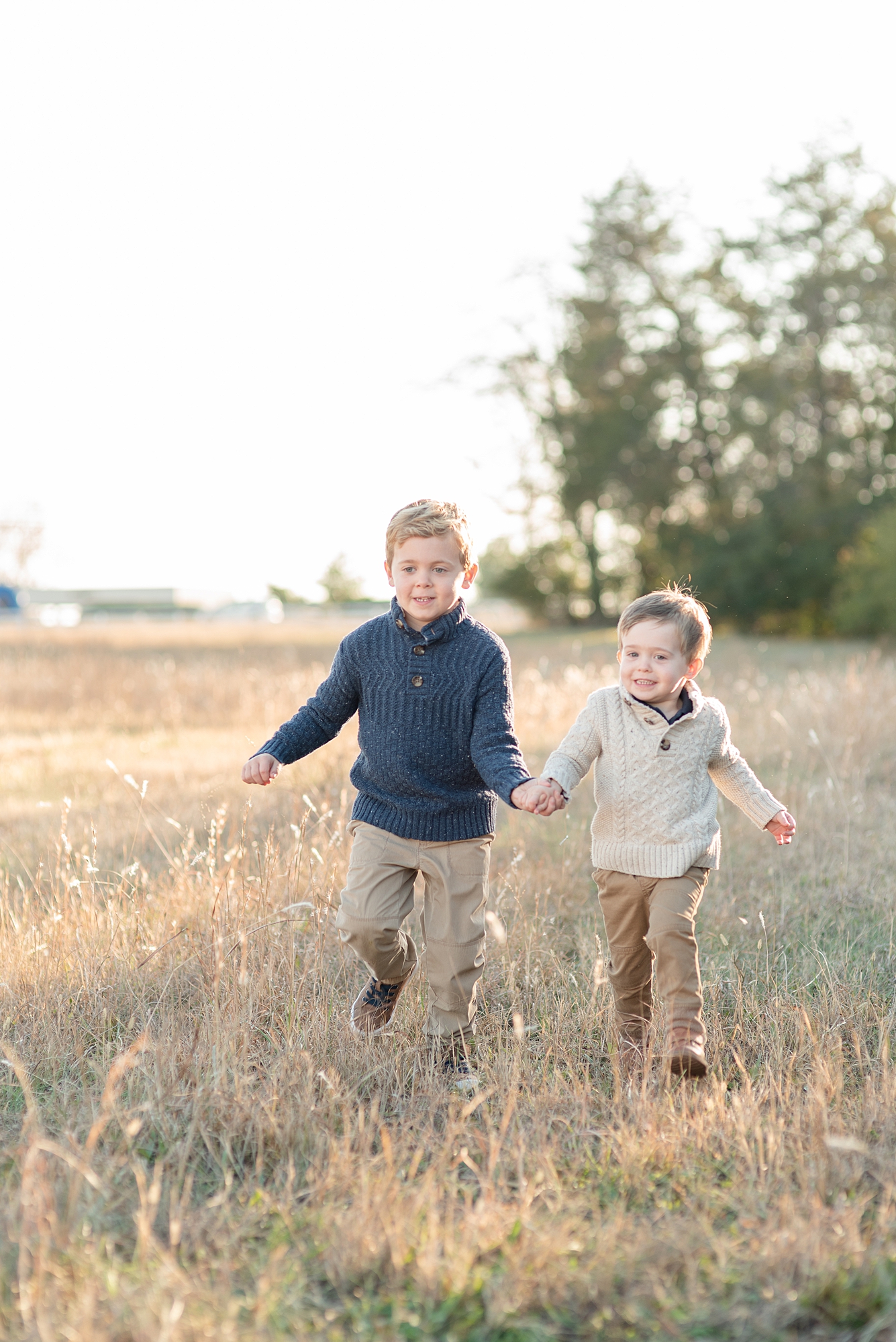 two brothers are holding hands and running in a field towards the photographer by Nashville family photographer Dolly DeLong Photography
