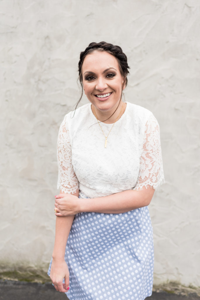 woman wearing a lace top with a polka dot blue dress is smiling at the camera for her branding session