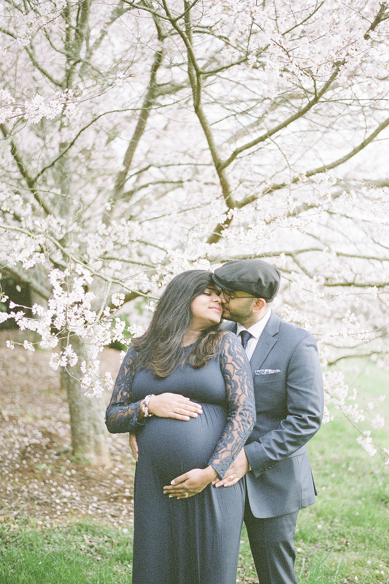 an indian couple are having their maternity session done on fuji400h film by Nashville family photographer Dolly DeLong Photography in Spring near spring blossom trees
