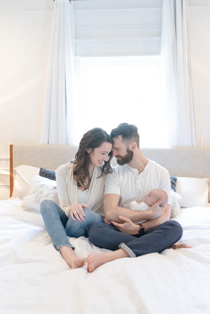 a mom and dad are sitting on their bed in east nashville for their family session with Nashville newborn family photographer dolly delong photography