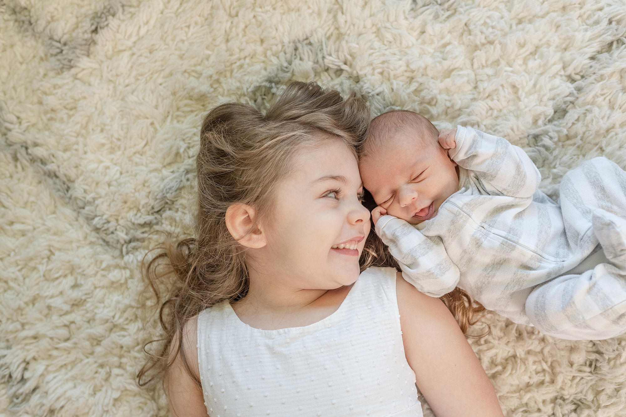 a newborn brother and big sister are laying side by side on the carpet and smiling for family photos by nashville family photographer dolly delong photography