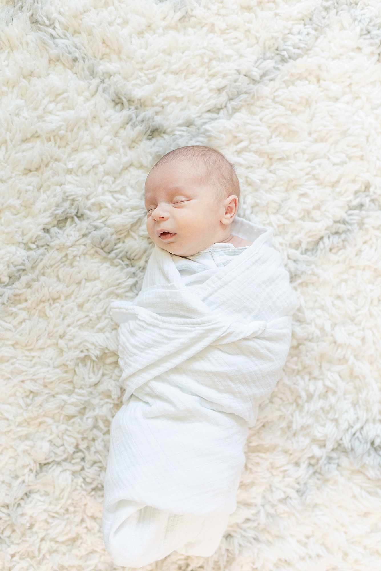 a newborn baby boy wrapped in a white swaddle while laying on a rug by nashville family photographer dolly delong photography