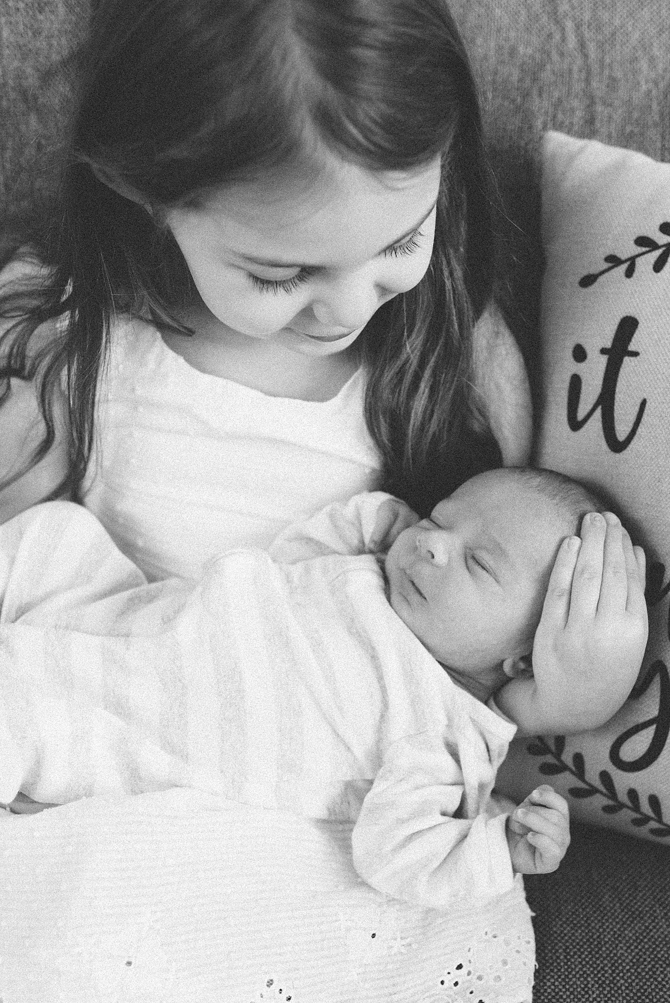 a black and white photo of a big sister holding her baby newborn brother by nashville family photographer dolly delong photography