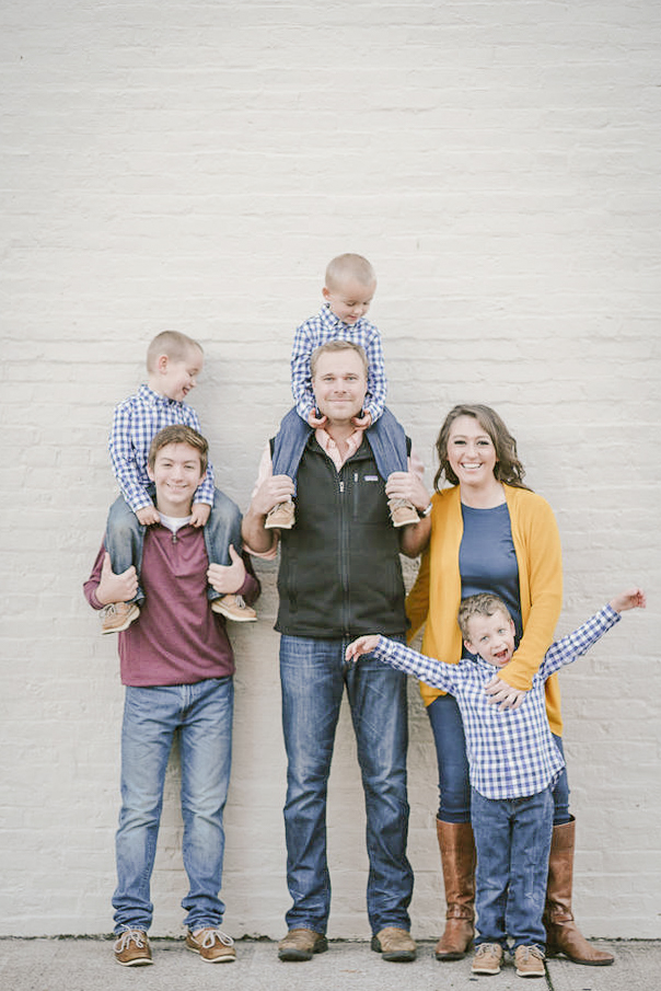 family of six is standing against a white backdrop wall in downtown franklin Tennessee for family photos by Nashville Family Photographer Dolly DeLong Photography