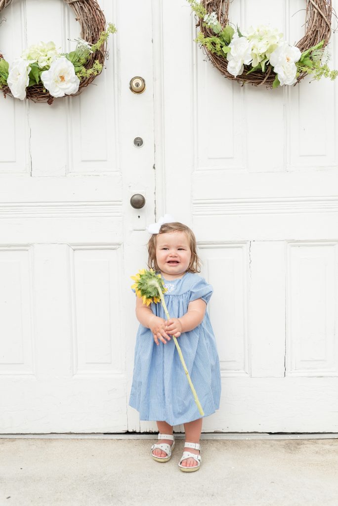 little girl holding a sunflower and standing against big white church doors in downtown franklin tennessee by Nashville family photographer Dolly DeLong PHotography
