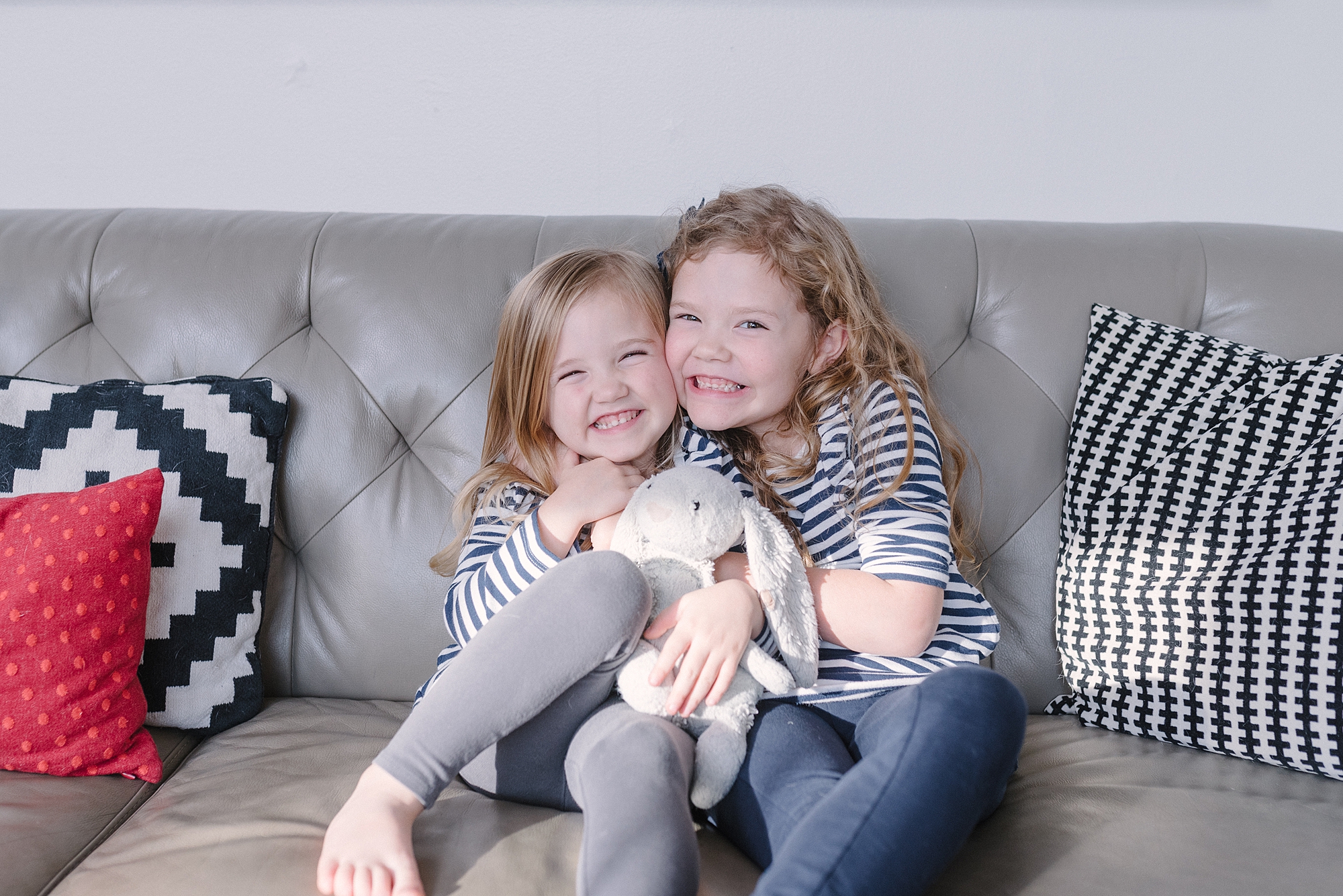 two sisters smiling on sofa for family photos by Nashville Family Photographer Dolly DeLong Photography