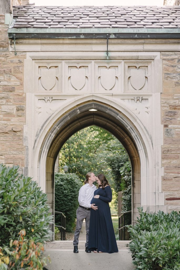 A husband and wife are standing under the archway at Vanderbilt University for their maternity session by Nashville Maternity Photographer Dolly DeLong Photography Summer 2020
