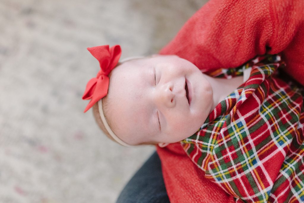 newborn baby girl wearing a plaid christmas baby wrap swaddle and smiling at the camera while sleeping by Nashville family photographer Dolly DeLong Photography