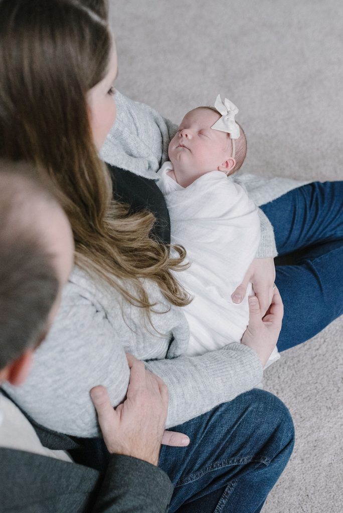 a mom and a dad are sitting on the floor of their daughter's nursery and holding their newborn daughter by Nashville newborn photographer and Nashville family photographer Dolly deLong Photography