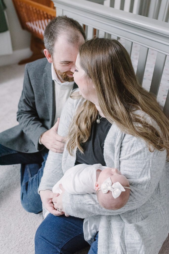 a mom and a dad are sitting on the floor of their daughter's nursery and holding their newborn daughter by Nashville newborn photographer and Nashville family photographer Dolly deLong Photography