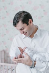 dad holds baby girl in arms during newborn photos at home